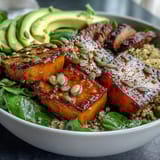 Golden, caramelized butternut squash and tender sliced steak sit atop a bed of greens and quinoa, ready for dinner.