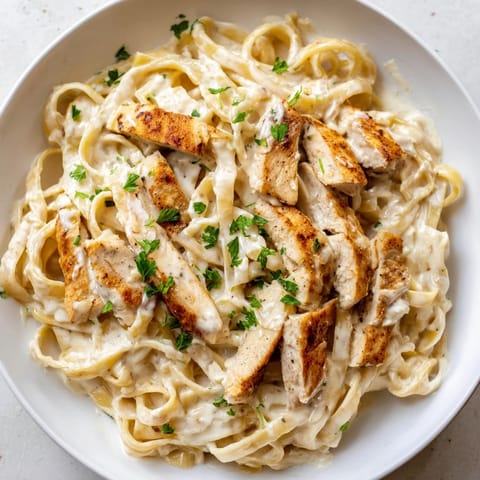Golden Cajun Chicken Alfredo in a white bowl, sauce glistening on fettuccine noodles.