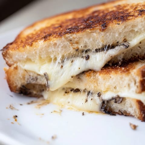 A close-up of a Truffle Grilled Cheese sandwich, showcasing the gooey cheese pull and buttery, toasted crust of the artisan bread.  
