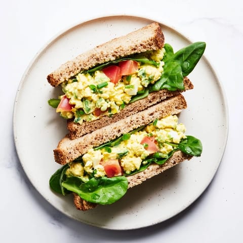 A close-up view of creamy avocado egg salad spread thickly on bread, garnished with chopped chives.  