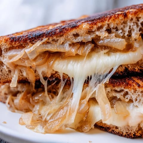 A gourmet Caramelized Onion & Gruyère Grilled Cheese sandwich served with a side of fresh greens.