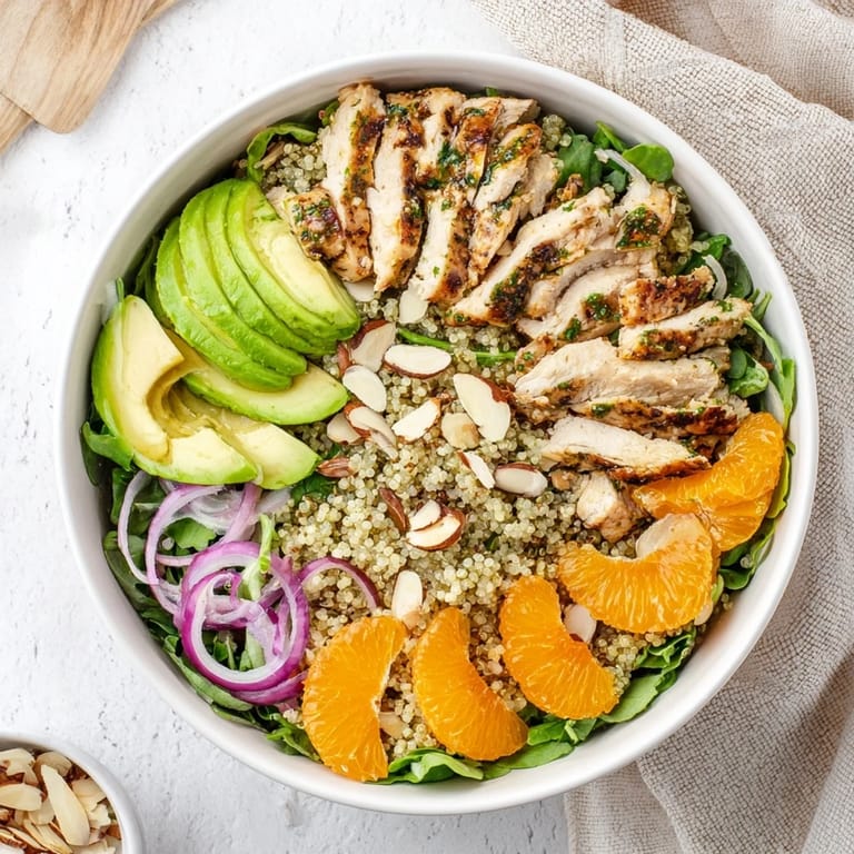 A close-up of the Citrus Herb Chicken Salad Bowl shows herb-marinated chicken, sliced avocado, and toasted almonds with zesty vinaigrette.  