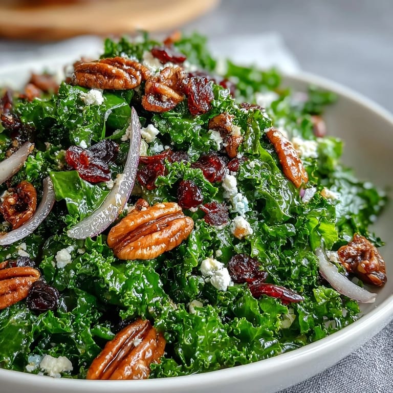 Hearty maple mustard kale salad tossed with red onion slices and crumbled feta, served warm on a rustic white platter.