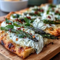 Roasted asparagus flatbread with burrata and lemon, topped with fresh basil and chili flakes for a vibrant appetizer.